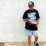 Person wearing a interpretation of art design on black t-shirt and denim shorts, standing on a concrete surface.