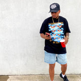 Person wearing a interpretation of art design on black t-shirt and denim shorts, standing on a concrete surface.