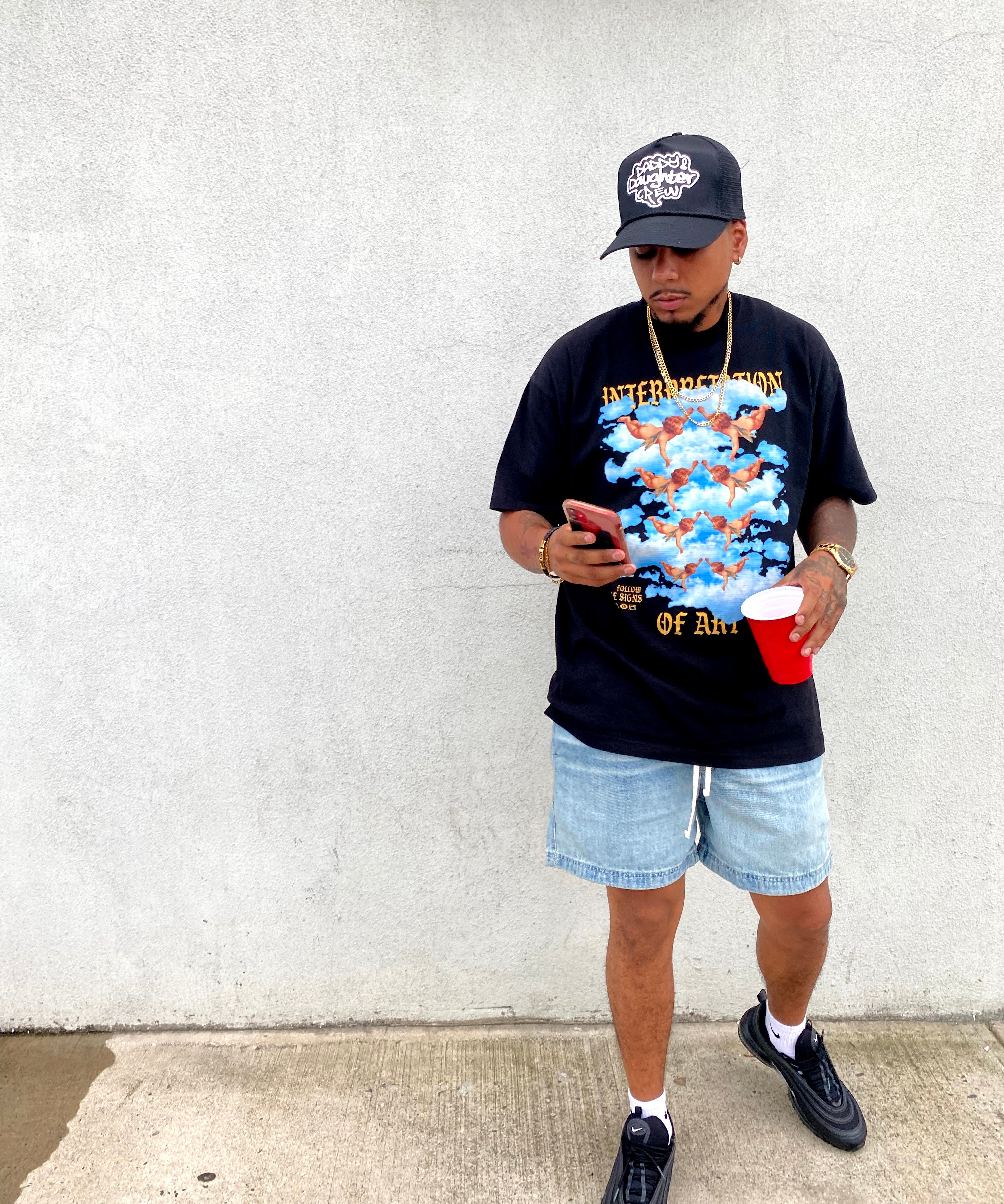 Person wearing a interpretation of art design on black t-shirt and denim shorts, standing on a concrete surface.