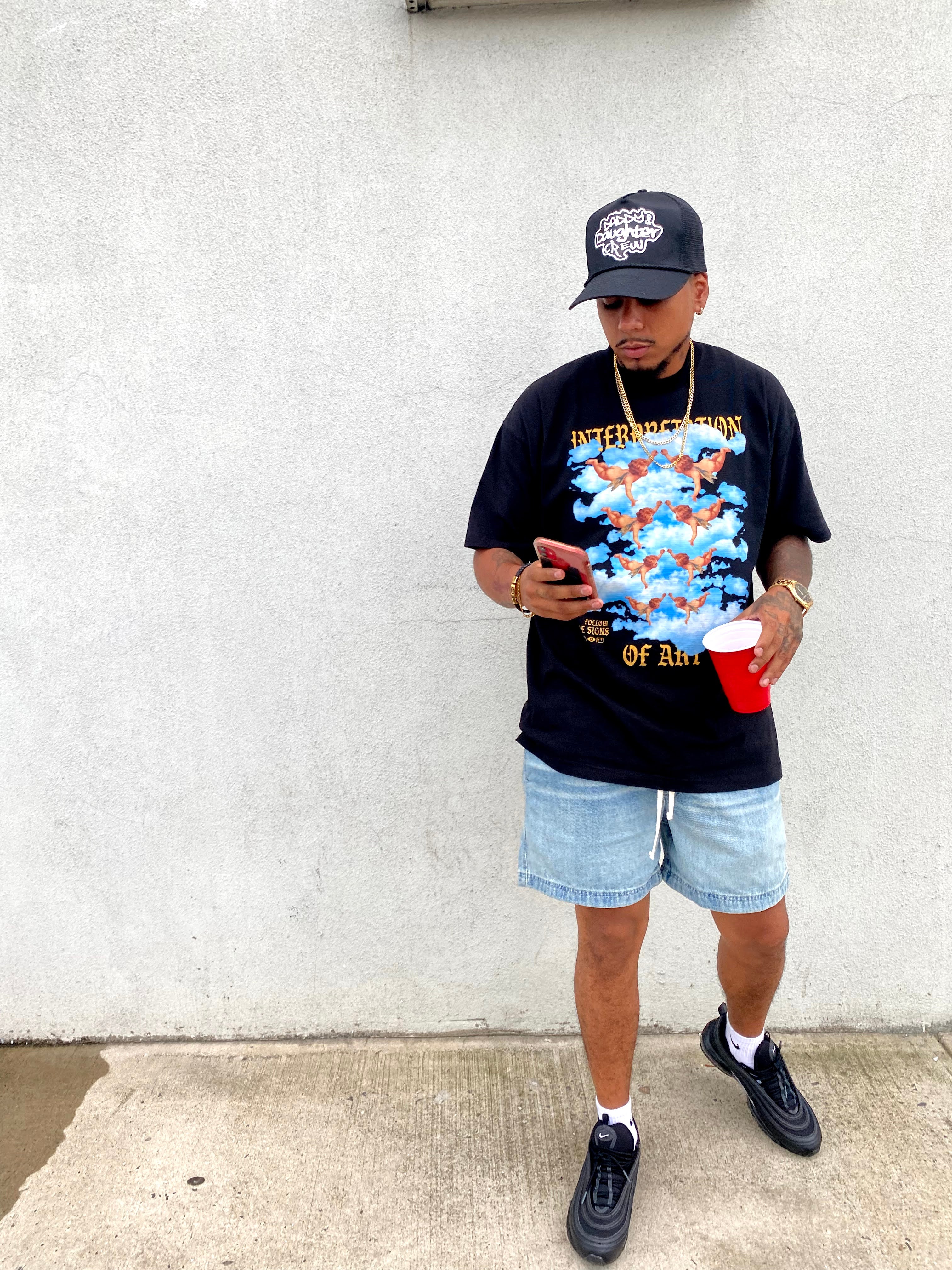 Person wearing a interpretation of art design on black t-shirt and denim shorts, standing on a concrete surface.